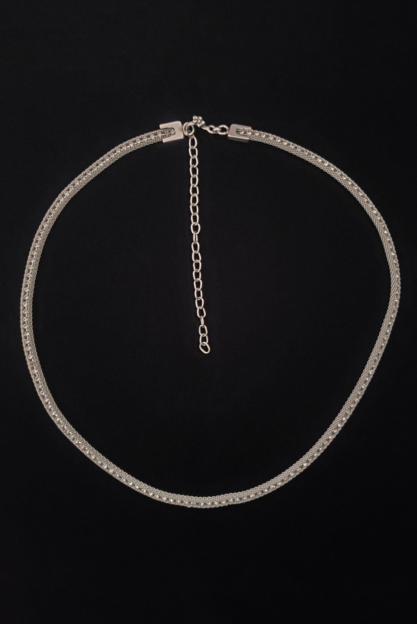 Vertical top view of 1960s vintage adjustable silver tone metal mesh and rhinestone chain belt with floral hook, size medium to large.