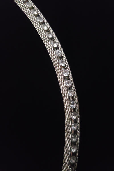 Detail view of 1960s vintage adjustable silver tone metal mesh and rhinestone chain belt with floral hook, size medium to large. Showing a close up of the metal mesh with a line of clear round rhinestones in the center.