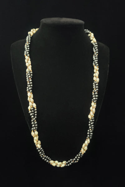 Vertical view of 1980s vintage white freshwater pearl, gray hematite, and gold tone beaded twisted triple strand long necklace. Shown on a stand.