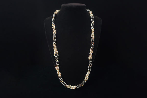 Horizontal view of 1980s vintage white freshwater pearl, gray hematite, and gold tone beaded twisted triple strand long necklace. Shown on a stand.