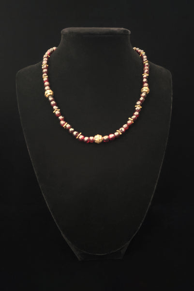 Vertical front view of 1970s vintage dark red garnet and brass beaded necklace. Showing the necklace on a display stand.