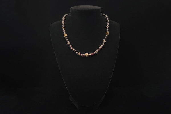 Horizontal front view of 1970s vintage dark red garnet and brass beaded necklace. Showing the necklace on a display stand.