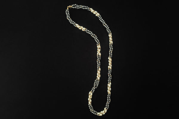 Horizontal view of 1980s vintage white freshwater pearl, gray hematite, and gold tone beaded twisted triple strand long necklace.