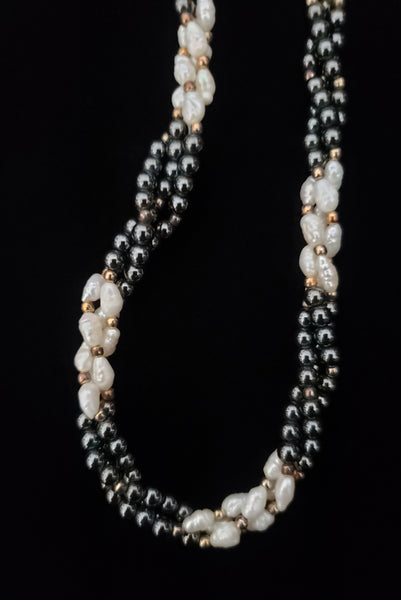 Detail view of 1980s vintage white freshwater pearl, gray hematite, and gold tone beaded twisted triple strand long necklace.