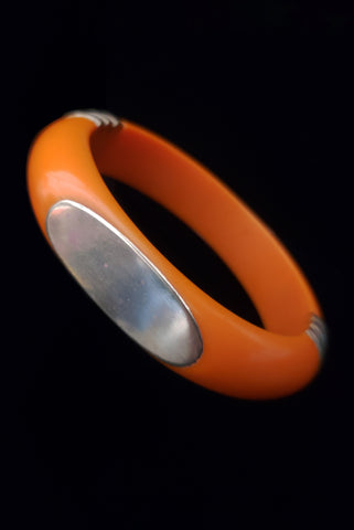 Vertical perspective view of 1970s vintage orange plastic and brass bangle bracelet, made in India.