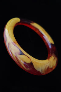 Vertical perspective view of 1960s vintage translucent orange and mustard marbled artisan asymmetrical bangle bracelet.