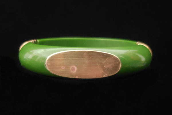 Horizontal front view of 1970s vintage green plastic and brass bangle bracelet, made in India. Showing some spots on the brass plate.