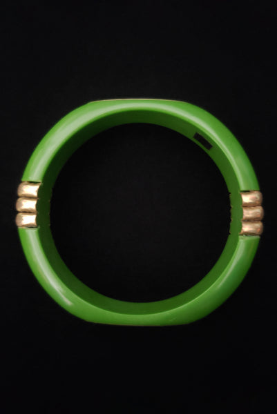 Vertical top view of 1970s vintage green plastic and brass bangle bracelet, made in India.