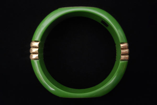 Horizontal top view of 1970s vintage green plastic and brass bangle bracelet, made in India.
