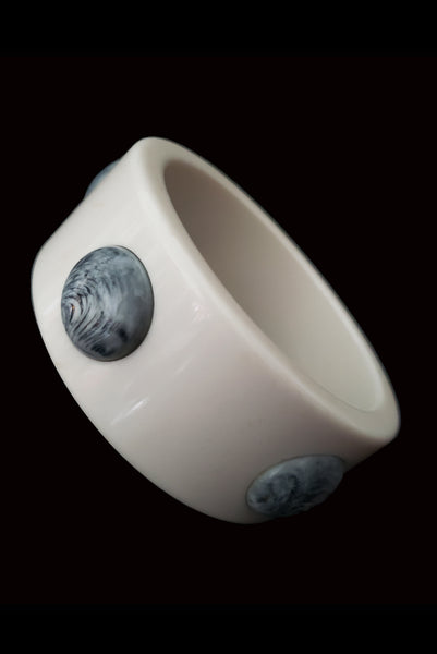 Vertical perspective view of 1960s vintage white Lucite plastic sliced bangle bracelet with raised gray marbled dots.