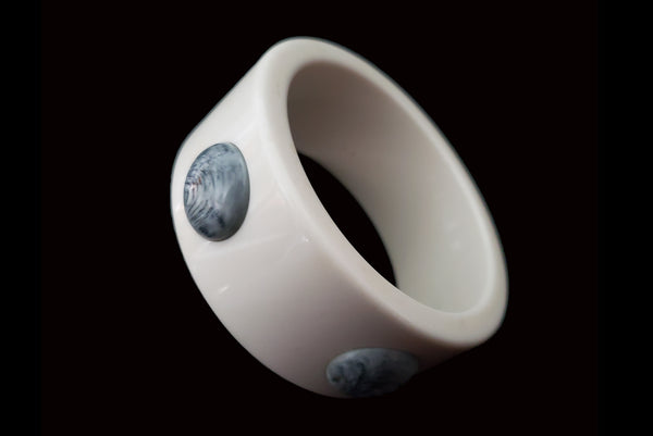 Horizontal perspective view of 1960s vintage white Lucite plastic sliced bangle bracelet with raised gray marbled dots.