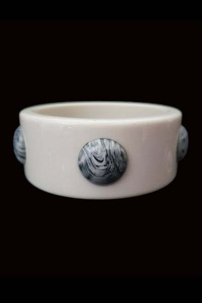 Vertical front view of 1960s vintage white Lucite plastic sliced bangle bracelet with raised gray marbled dots.