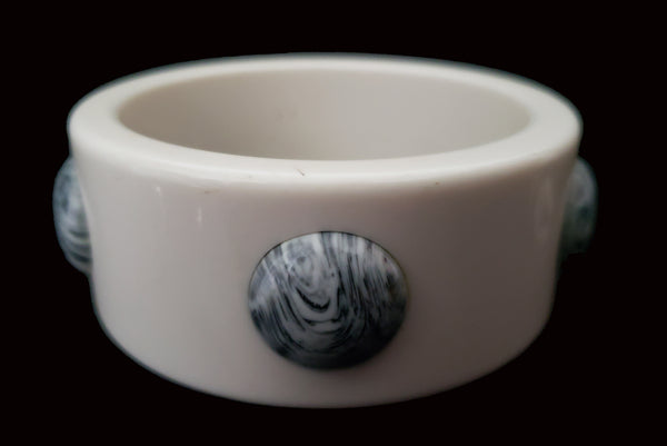 Horizontal front view of 1960s vintage white Lucite plastic sliced bangle bracelet with raised gray marbled dots.