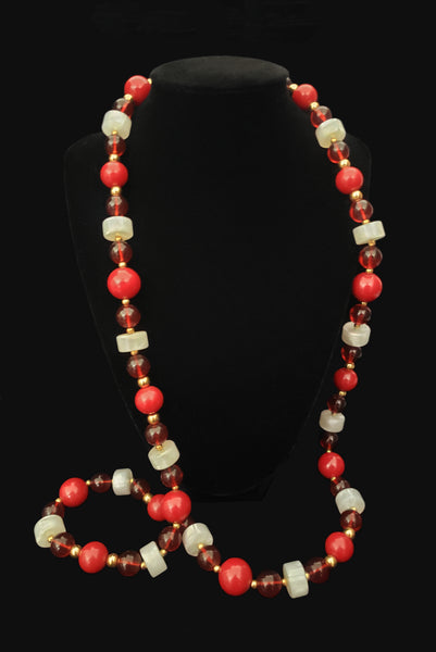Vertical view of 1960s vintage red & white Lucite plastic beaded long necklace with gold tone spacers by Monet. Showing the necklace on a display.