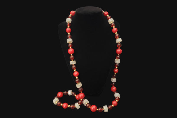 Horizontal view of 1960s vintage red & white Lucite plastic beaded long necklace with gold tone spacers by Monet. Showing the necklace on a display.