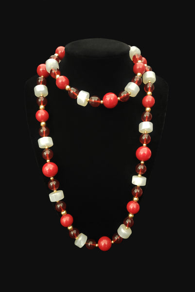 Vertical view of 1960s vintage red & white Lucite plastic beaded long necklace with gold tone spacers by Monet. Showing the necklace on a display.