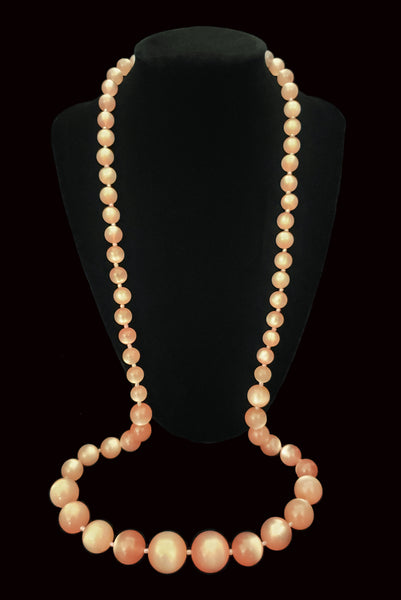 Vertical view of 1960s vintage long pink moonglow Lucite graduated bead necklace. Showing the necklace on a display.