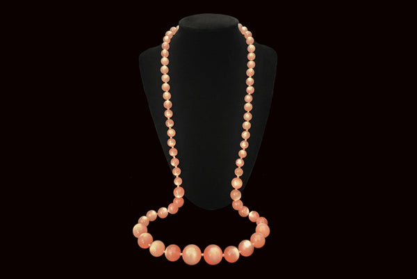 Horizontal view of 1960s vintage long pink moonglow Lucite graduated bead necklace. Showing the necklace on a display.
