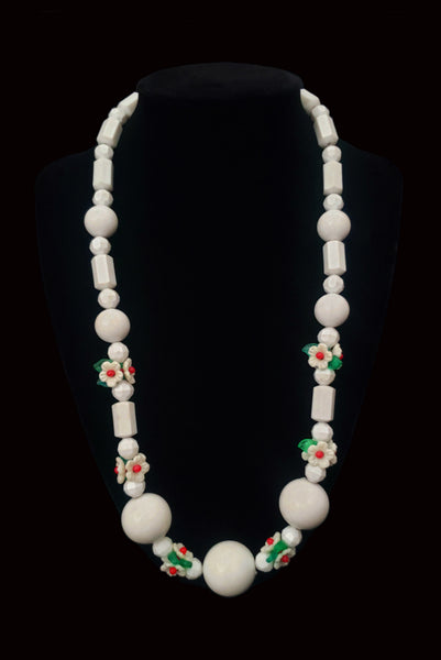 Vertical view of 1960s vintage green, red, and white floral bead plastic long necklace. Showing the necklace on a display.