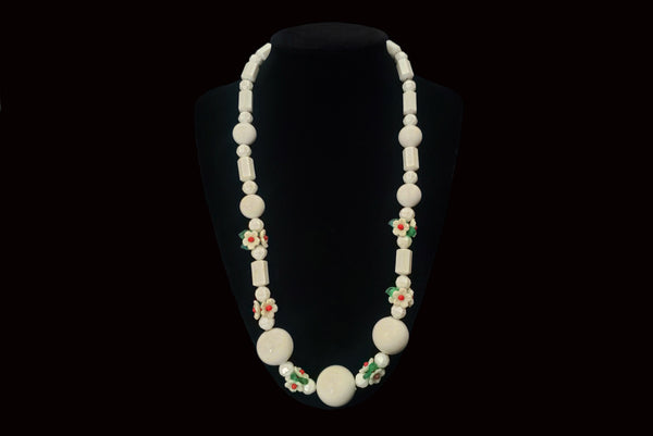 Horizontal view of 1960s vintage green, red, and white floral bead plastic long necklace. Showing the necklace on a display.