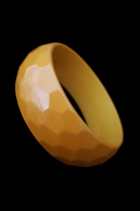 Vertical perspective view of 1930s vintage honeycomb faceted carved egg yolk/butterscotch yellow Bakelite bangle bracelet.