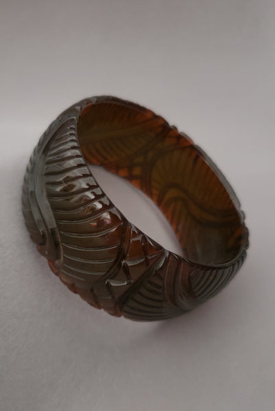 Vertical perspective view of 1930s vintage leaf carved green red prystal Bakelite statement bangle bracelet.