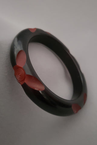 Vertical perspective view of 1940s vintage black resin washed floral carved dark red cut through Bakelite bangle bracelet.