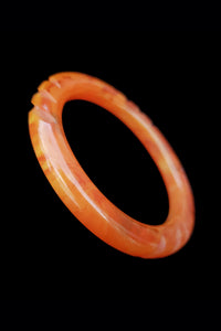 Vertical perspective view of 1940s vintage translucent orange marbled notch carved Bakelite tube bangle bracelet.