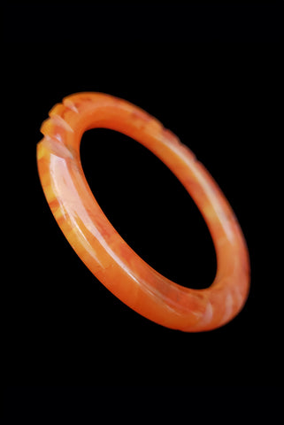 Vertical perspective view of 1940s vintage translucent orange marbled notch carved Bakelite tube bangle bracelet.