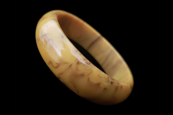 Horizontal perspective view of 1930s vintage cream corn yellow and chocolate brown marbled Bakelite bangle bracelet.