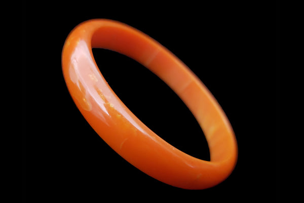 Horizontal perspective view of 1940s vintage slim domed orange marbled Bakelite bangle bracelet.
