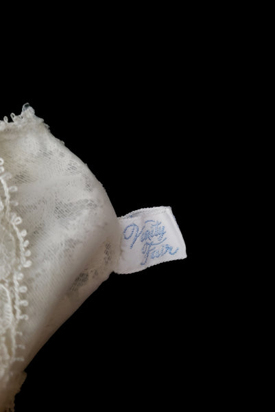 Interior detail view of 1950s vintage white sheer lace sweetheart neckline full slip by Vanity Fair, small to medium. Showing the Vanity Fair label.