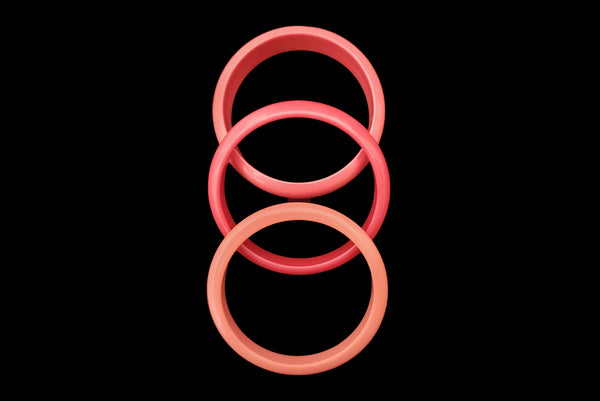 Horizontal top view of 1980s vintage coral pink plastic bangle bracelet set of three (3).