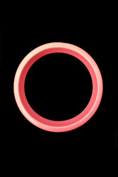 Vertical top view of 1980s vintage coral pink plastic bangle bracelet set of three (3). Showing the medium tone bangle on its own.