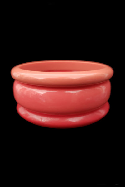 Vertical front view of 1980s vintage coral pink plastic bangle bracelet set of three (3).