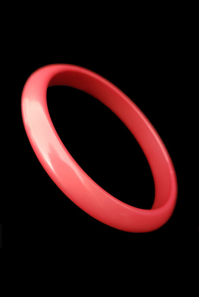 Vertical perspective view of 1980s vintage coral pink plastic bangle bracelet set of three (3). Showing the darkest bangle on its own.