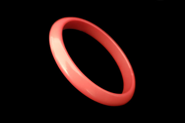 Horizontal perspective view of 1980s vintage coral pink plastic bangle bracelet set of three (3). Showing the darkest bangle on its own.