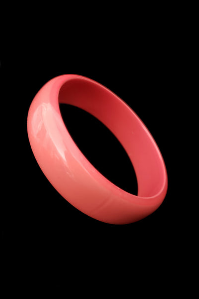 Vertical perspective view of 1980s vintage coral pink plastic bangle bracelet set of three (3). Showing the medium tone bangle on its own.