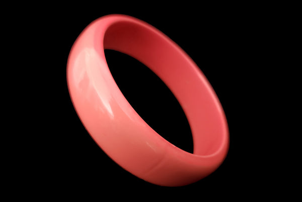Horizontal perspective view of 1980s vintage coral pink plastic bangle bracelet set of three (3). Showing the medium tone bangle on its own.
