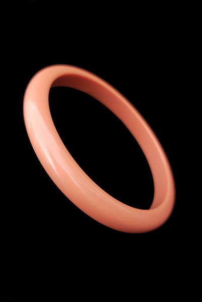 Vertical perspective view of 1980s vintage coral pink plastic bangle bracelet set of three (3). Showing the lightest bangle on its own.