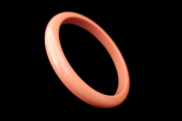 Horizontal perspective view of 1980s vintage coral pink plastic bangle bracelet set of three (3). Showing the lightest bangle on its own.