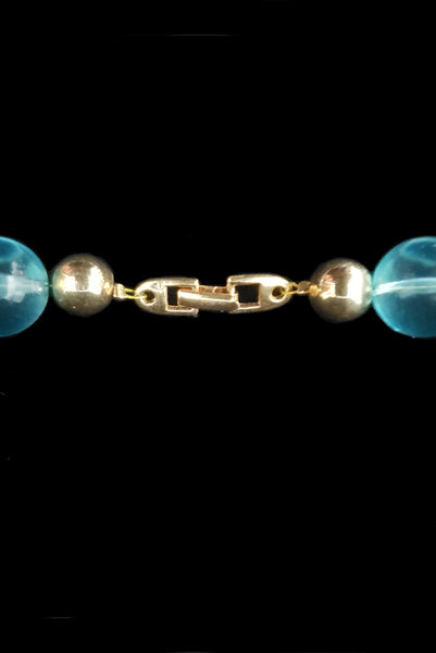Detail view of 1980s vintage transparent aqua blue Lucite plastic and gold tone metal large bead necklace by Napier. Showing a close-up of the gold tone clasp.