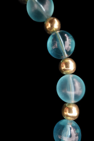 Detail view of 1980s vintage transparent aqua blue Lucite plastic and gold tone metal large bead necklace by Napier. Showing a close-up of the round beads.