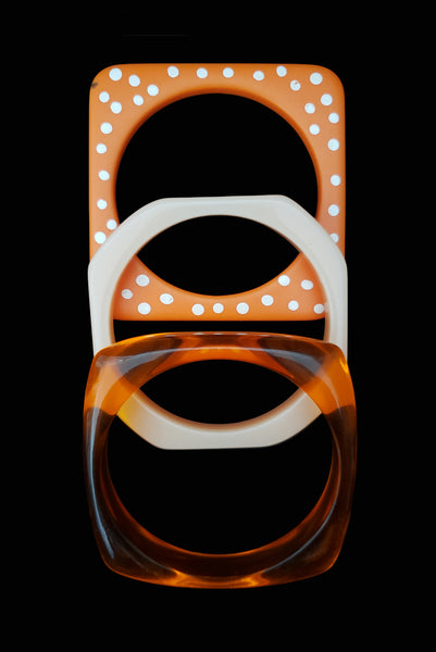 Vertical top view of 1980s vintage orange and white square sliced polka dot, striped, and translucent solid three (3) bangle bracelet set.