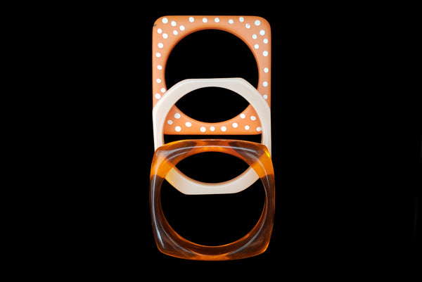 Horizontal top view of 1980s vintage orange and white square sliced polka dot, striped, and translucent solid three (3) bangle bracelet set.