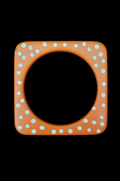 Vertical top view of 1980s vintage orange and white square sliced polka dot, striped, and translucent solid three (3) bangle bracelet set. Showing the orange with white polka dots bangle alone. It has a small dark mark on the front corner.