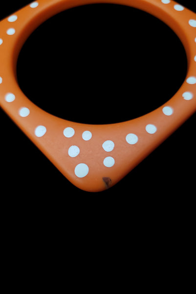 Detail view of 1980s vintage orange and white square sliced polka dot, striped, and translucent solid three (3) bangle bracelet set. Showing the orange with white polka dots bangle alone. It has a small dark mark on the front corner.