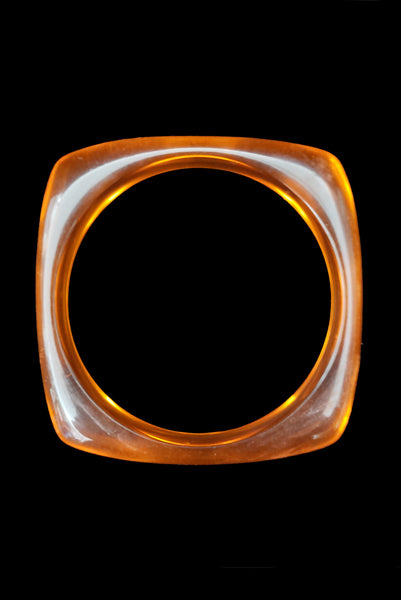 Vertical top view of 1980s vintage orange and white square sliced polka dot, striped, and translucent solid three (3) bangle bracelet set. Showing the orange translucent bangle alone.