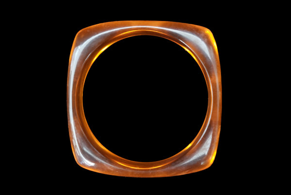 Horizontal top view of 1980s vintage orange and white square sliced polka dot, striped, and translucent solid three (3) bangle bracelet set. Showing the orange translucent bangle alone.
