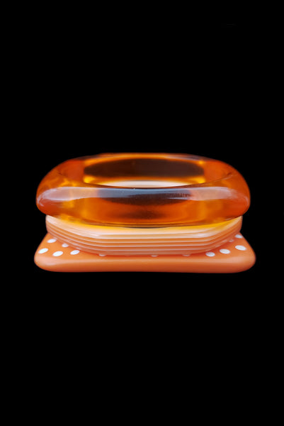 Vertical front view of 1980s vintage orange and white square sliced polka dot, striped, and translucent solid three (3) bangle bracelet set.